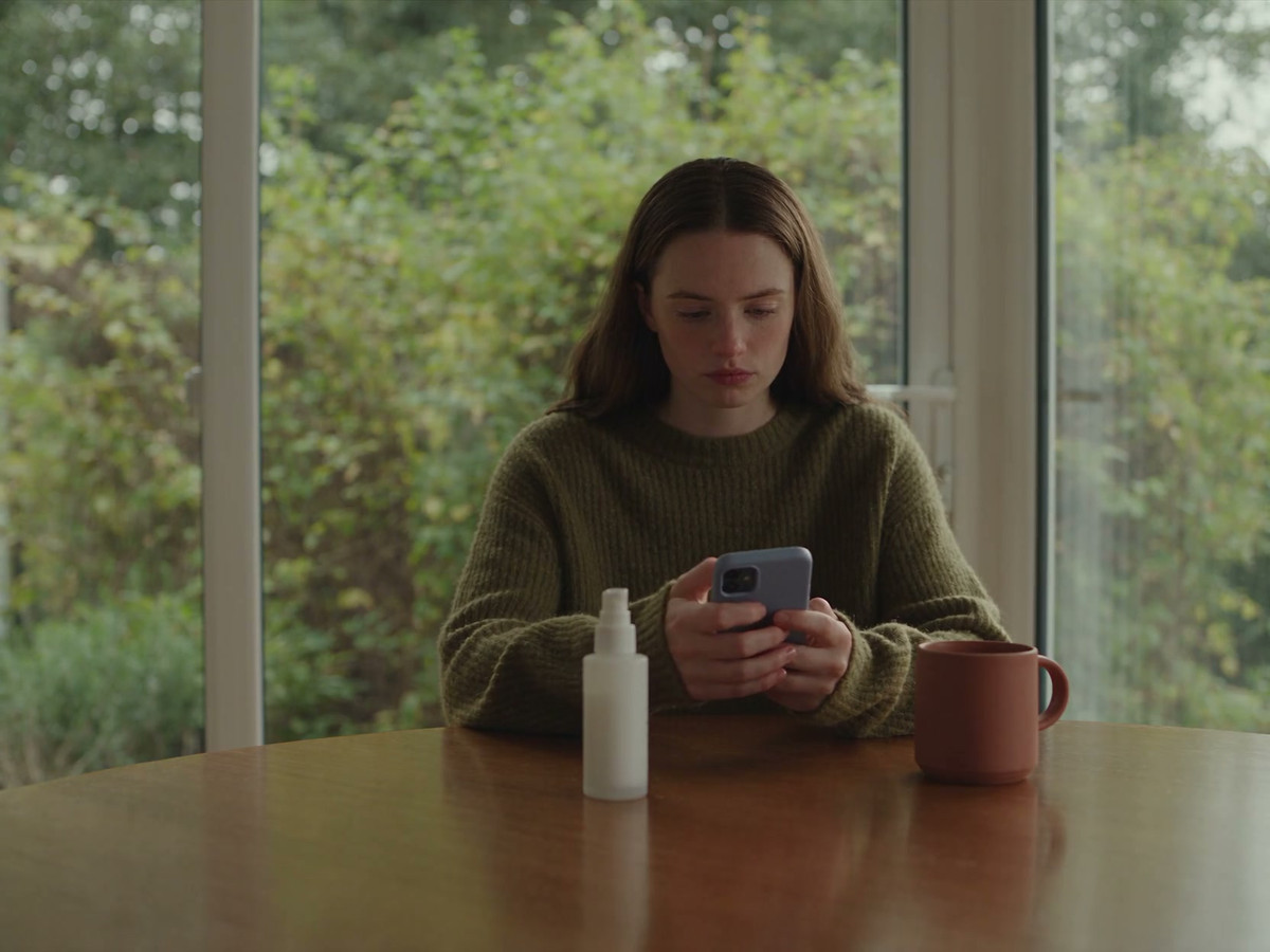A woman browses products on her phone at a sunny home table