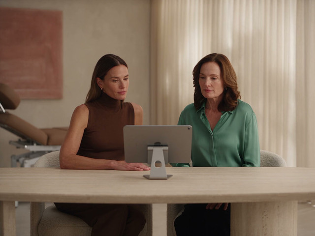 Two women reviewing a tablet at a clinic consultation table.